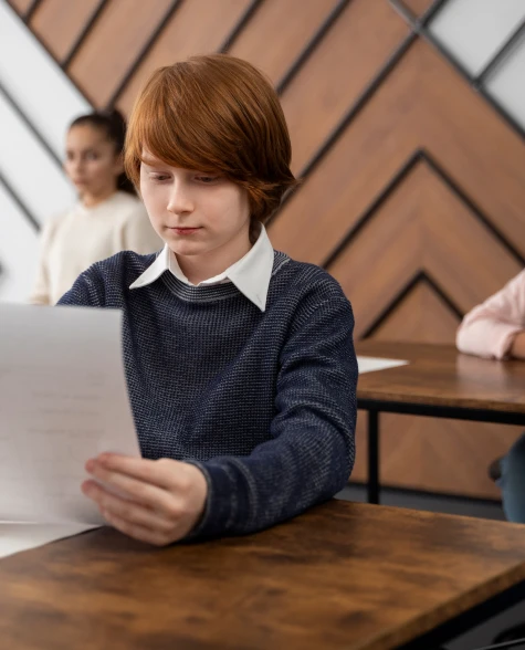 meninp ruivo sentado na sala de aula segurando um papel